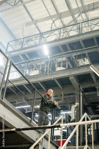 Bald mature engineer or foreman in workwear standing over staircase in factory © pressmaster