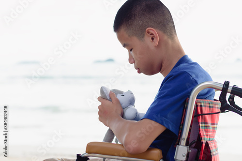 Asian special child on wheelchair is smiling, playing and doing activity on the sea beach, Lifestyle of disability child, Life in the education age, Happy disabled kid in travel holidays concept.