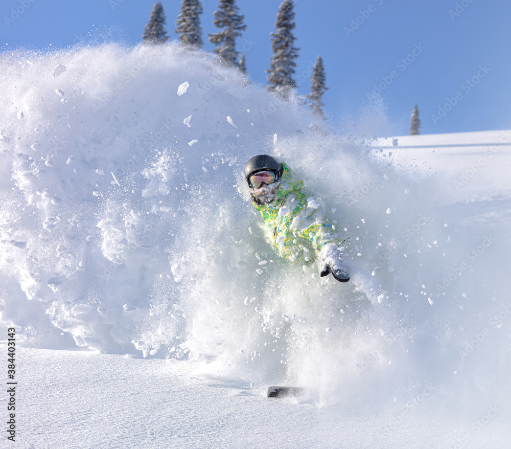 heliski snowboarding. freerider in a bright suit rides snowboarding with large splashes of snow on a sunny day. Young snowboarder. concept snowboard. big swirls of fresh snow in Good powder day