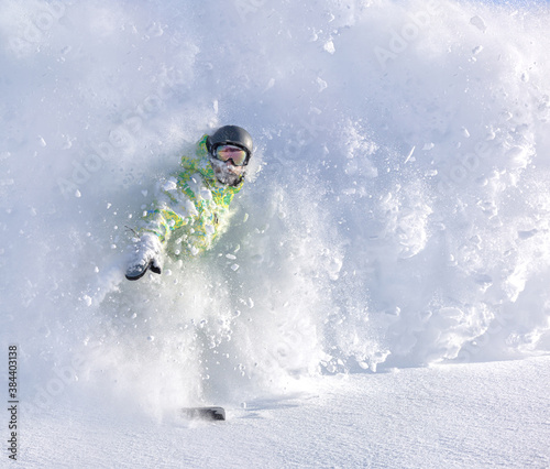 a fun snowboarder with a big mustache blows up a snow powder and raises a beautiful snow cloud. bright green and yellow overalls and a black helmet with a multi-colored mask. heliski snowboarding