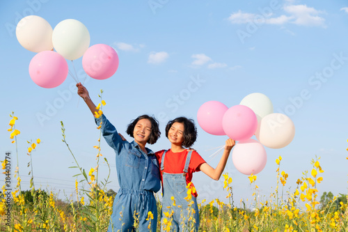 Two happy young girl hold wear jean hold balloon standing at yellow flower pakr with blue sky. photo