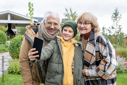 Happy schoolboy making selfie with his cheerful and affectionate grandparents © pressmaster
