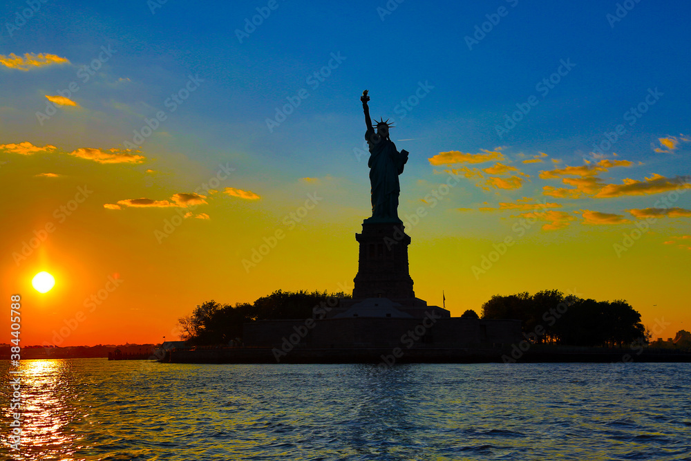 Statue of Liberty in silhouette at sunset viewed from the water with clouds and colorful sky. Statue of Liberty in silhouette at sunset viewed from the water with clouds and colorful sky.