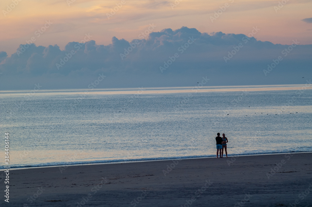 Ein Liebespaar als Silhouette am Meer vor einem dramatischen Himmel im Hintergrund