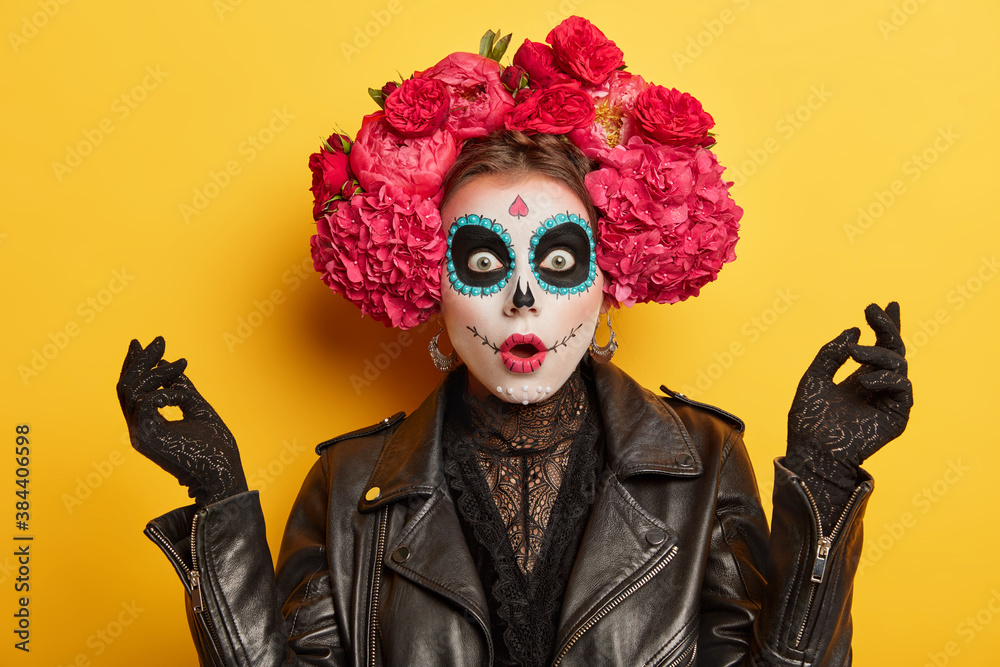 Scared emotional woman wears scary makeup and floral headwear stares