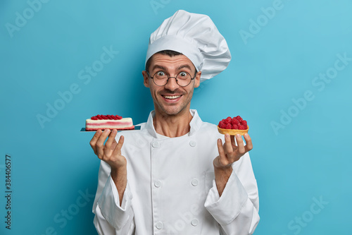 Slika na platnu Positive professional confectioner holds tasty handmade desserts with berries we