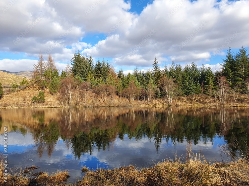 Scottish West Highland Way lake with forest reflection and blue cloudy sky