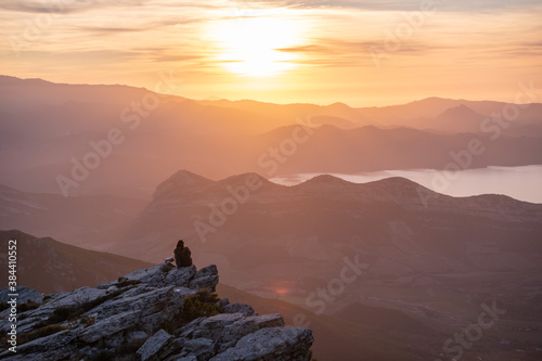 Fotografie Young woman enjoying beautiful sunset scenery from the peak of a mountain