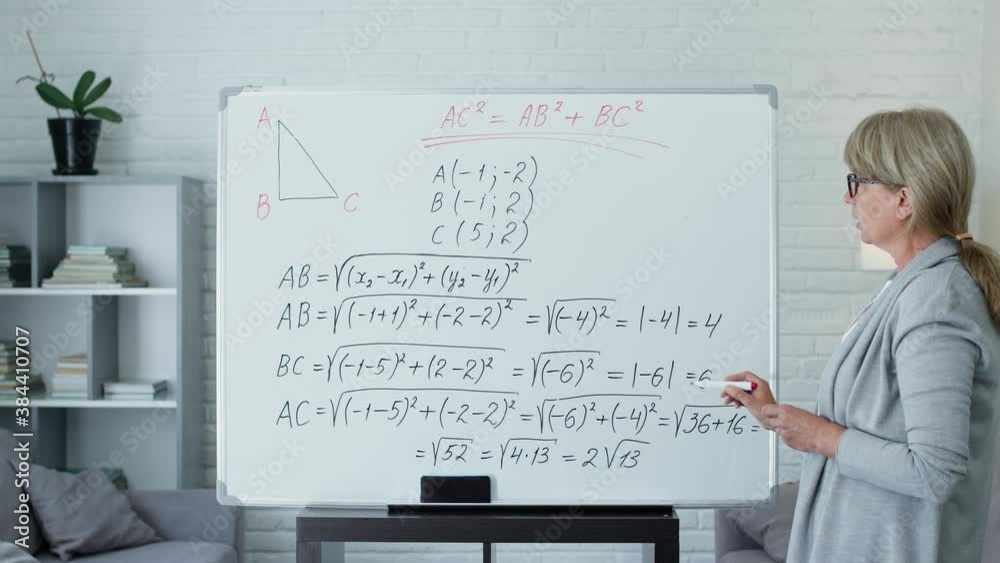 Female Math Teacher With Board Room With Board To Write Math Formulas. Woman Is Studying Online Or Recording Video Lesson. Female Math Teacher With Board Room With Board To Write Math Formulas. Woman Is Studying Online Or Recording Video Lesson.