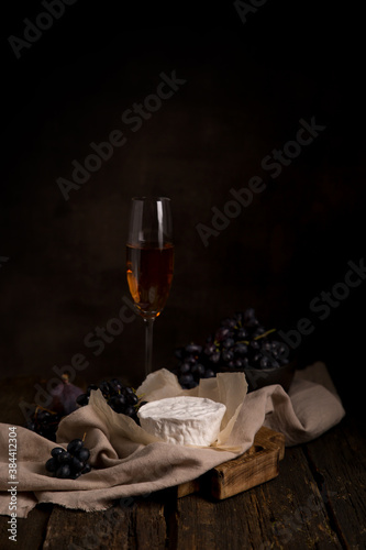 brie cheese, camembert cheese with grapes, a glass of wine on a dark table. Still life with cheese. Copy space vertically. Dark background