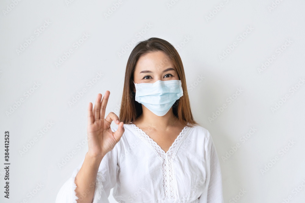 Closeup of beautiful young Asian girl with protective face mask showing fine in sign language hand and smiling at camera on white background. new normal, health care concept. Closeup of beautiful young Asian girl with protective face mask showing fine in sign language hand and smiling at camera on white background. new normal, health care concept.
