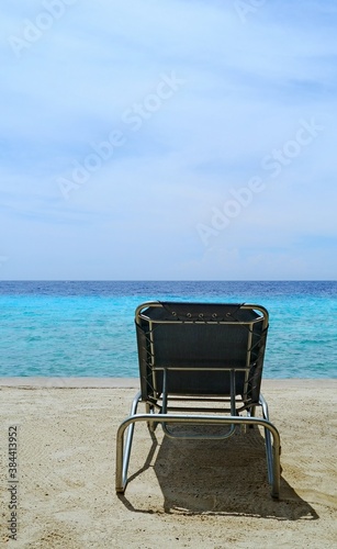 Empty lawn chair at the beach with turquoise ocean water and sky in the background © skyf