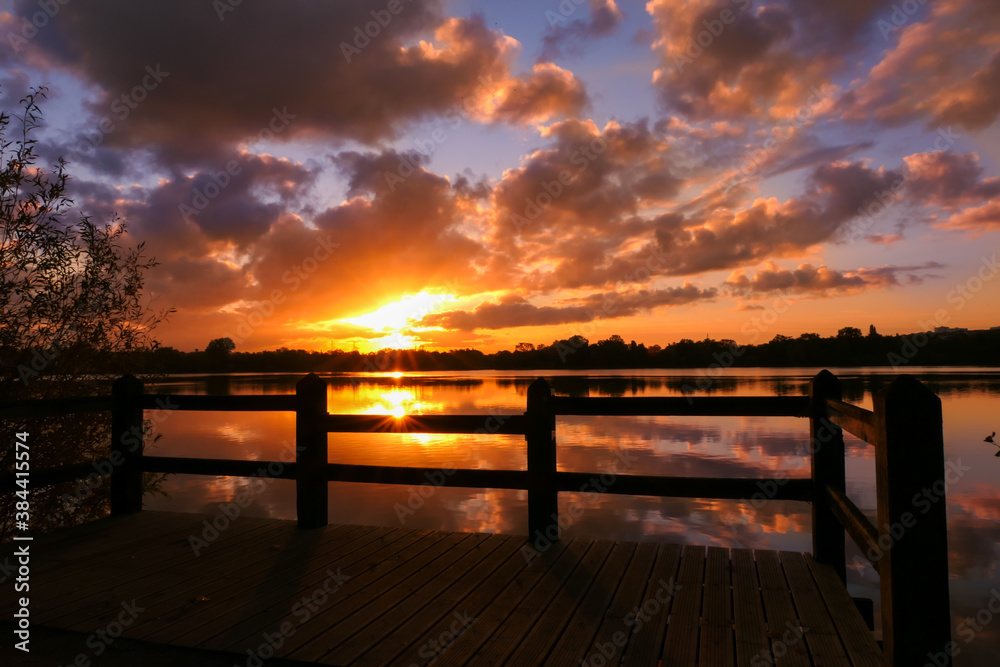 Amazing sunrise in rural scene. Symmetry of the sky in a lake at sunset. Clouds reflecting on the water. Quiet relaxing scene with a beautiful colorful cumulonimbus. Wooden pontoon in the foreground.