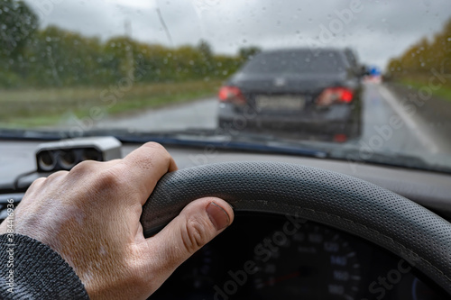 the driver's hand on the steering wheel of the car against the background of the car in front, which is waiting for the signal to avoid an obstacle due to road repairs in rainy cloudy weather in the a