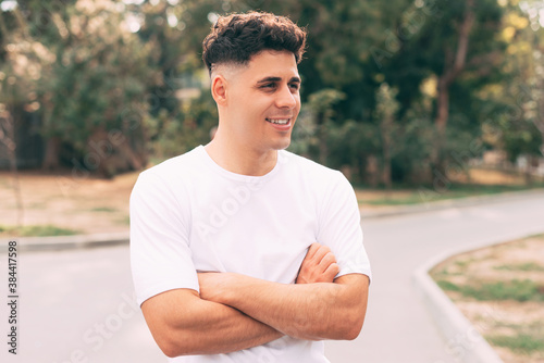 Photo of young handsome man standing outdoor with crossed arms and looking away and smiling