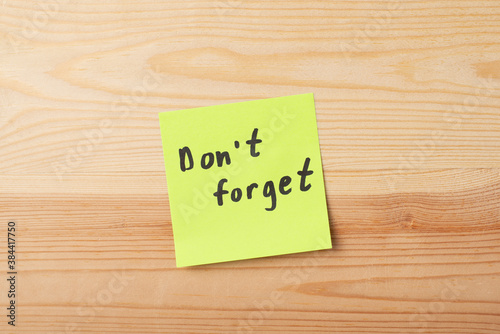 Sticky note with inscription DON`T FORGET on wooden table