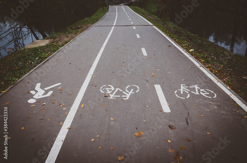 View of empty road in park marked with white pedestrian and bicycle signs during cloudy october day