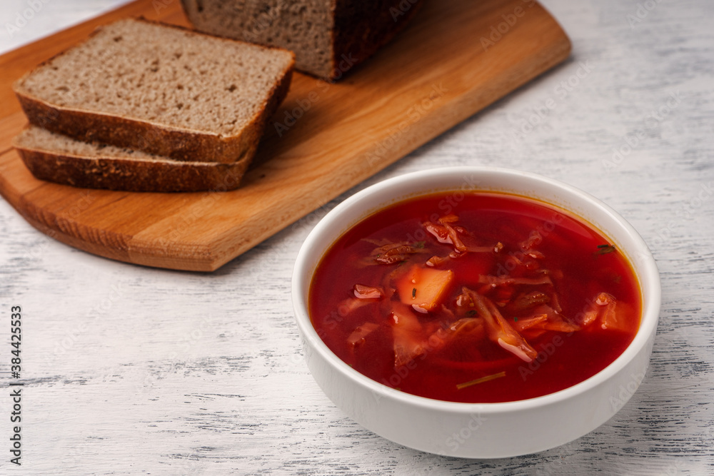 Vegetarian borscht in a white tureen on a light wooden table next to slices of wholemeal bread. Vegetarian borscht in a white tureen on a light wooden table next to slices of wholemeal bread.