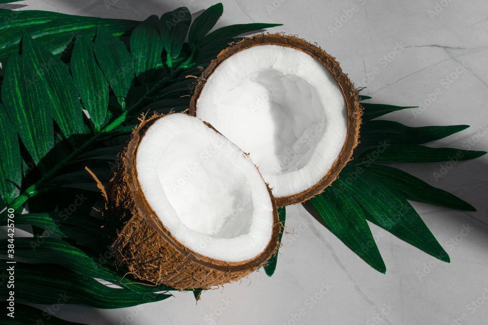 Two halves of coconut and tropical leaves, on a white background in the sun. The concept of vegetarianism and healthy food. selective focus