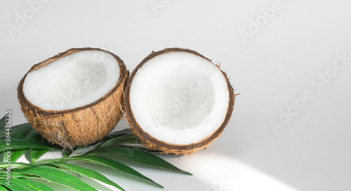 Two halves of coconut and tropical leaves, on a white background. Healthy food. Copy space