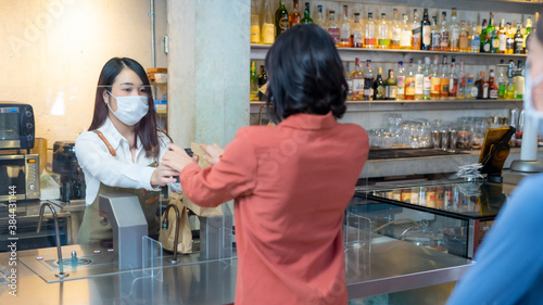 Asian female staff in uniform send disposable bag and cup to customer.