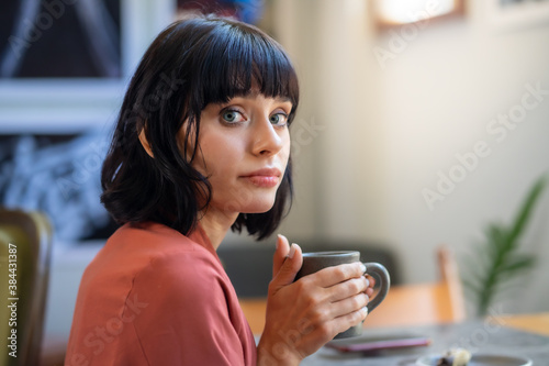 Caucasian female model holding a dark grey cup with 2 hands and look.