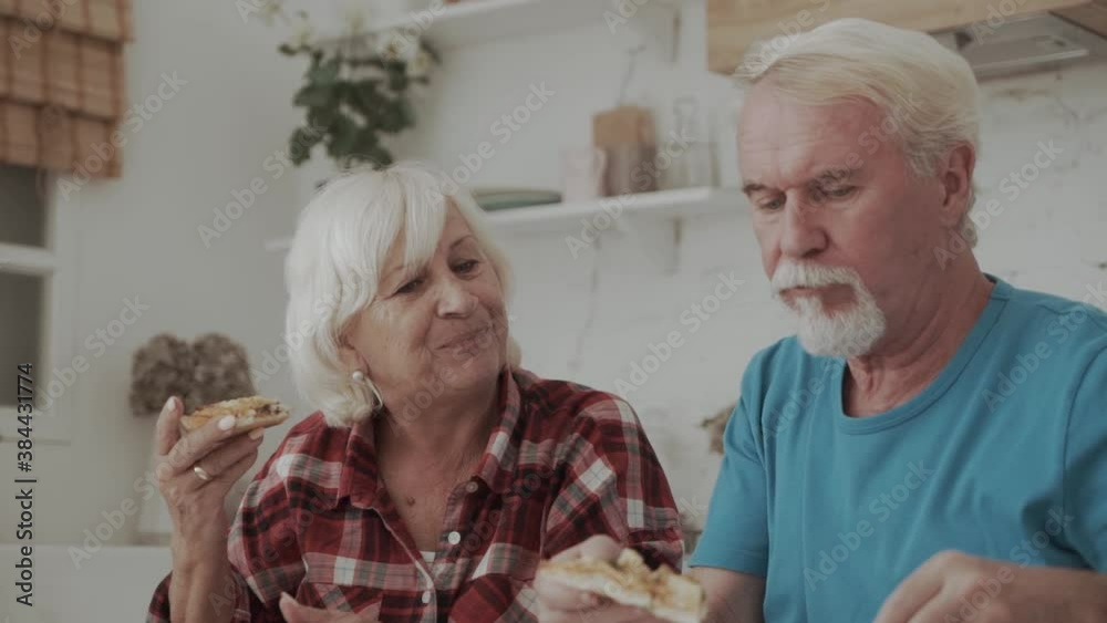 Mature couple eating delicious pizza in the kitchen. Man and woman hand-feed each other Mature couple eating delicious pizza in the kitchen. Man and woman hand-feed each other