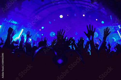 Abstract blur atmosphere: happy people enjoying outdoor music festival concert, raised up hands and clapping of pleasure, active night life concept, play of light and shadow on the stage