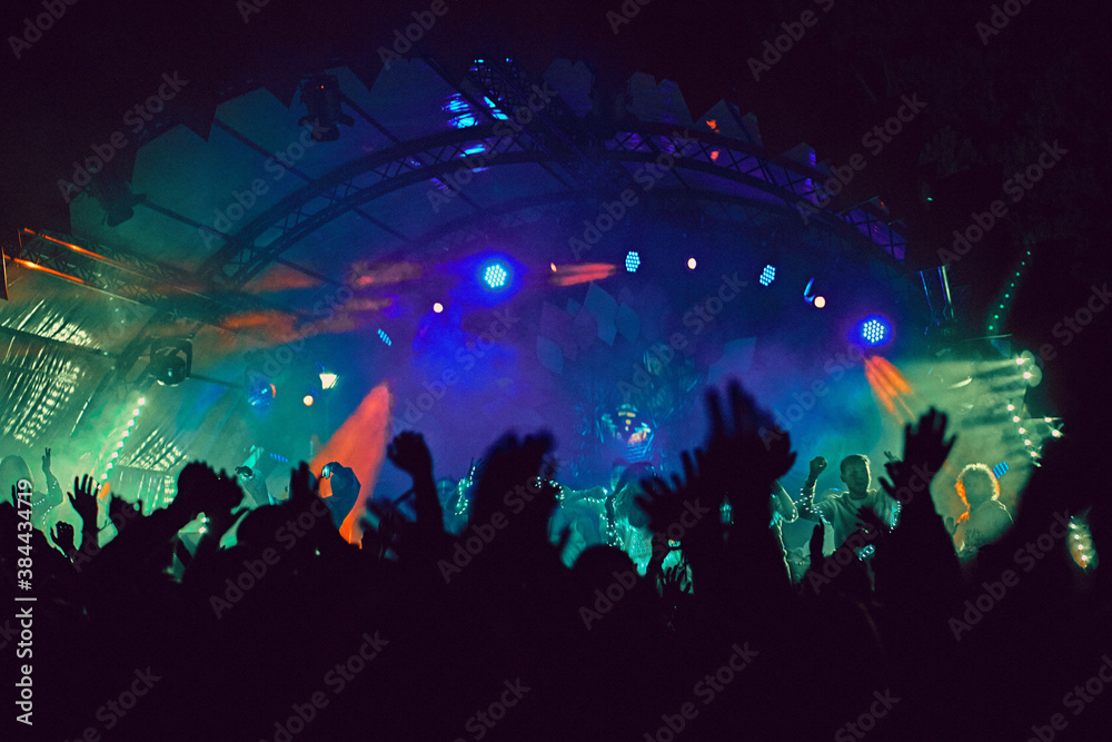 Abstract blur atmosphere: happy people enjoying outdoor music festival concert, raised up hands and clapping of pleasure, active night life concept, play of light and shadow on the stage