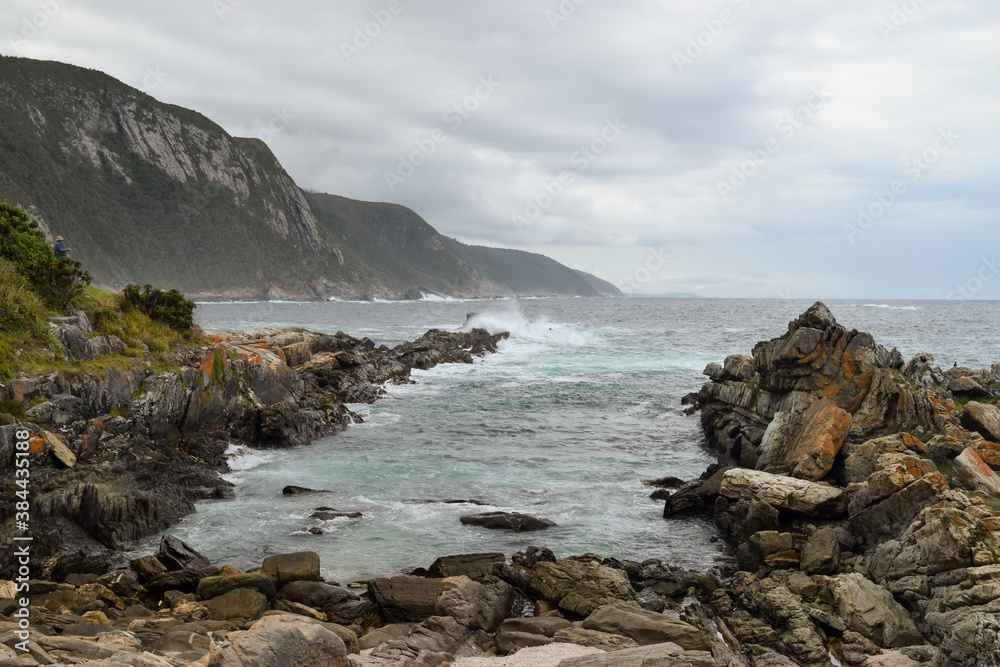 Obraz premium Waves hitting the rocks on a cloudy day. 
