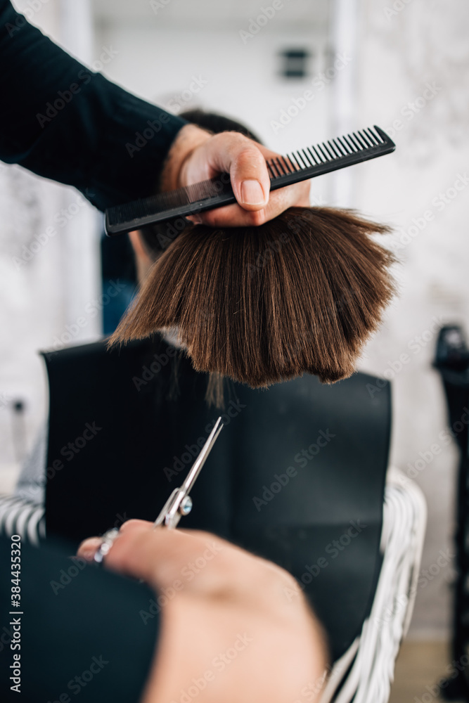 Naklejka premium Young girl enjoying at hairstyle treatment while professional hairdresser gently working and cutting her hair.