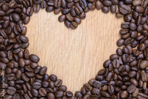A heart is laid out on a wooden surface made of coffee beans. In the center there is a void for the inscription.