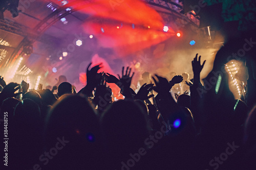Abstract blur atmosphere: happy people enjoying outdoor music festival concert, raised up hands and clapping of pleasure, active night life concept, play of light and shadow on the stage