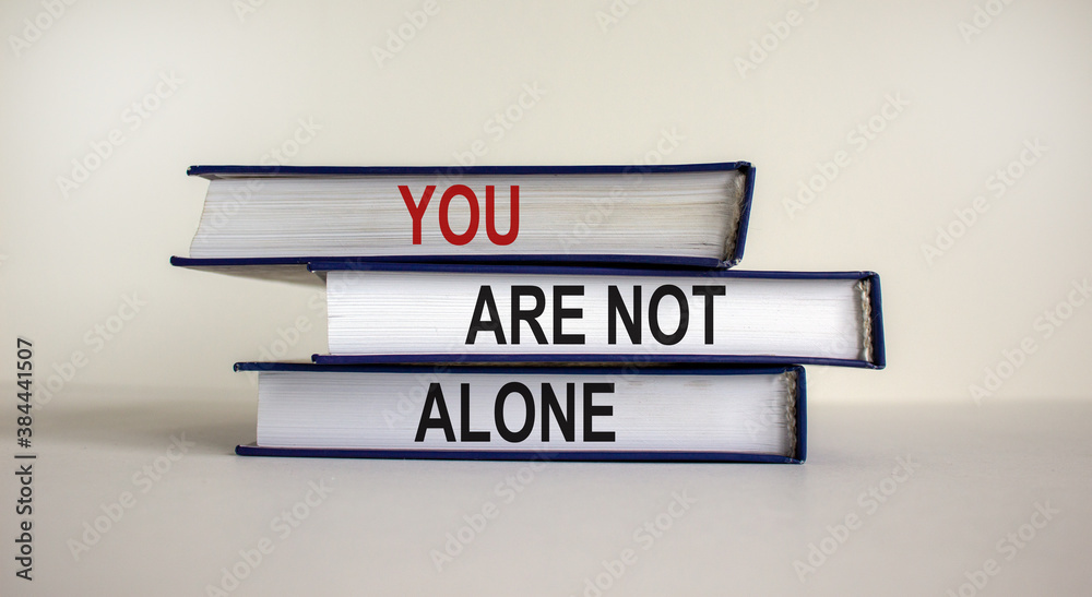 Books with text 'you are not alone' on beautiful white table. White background. Business and motivational concept. Copy space.