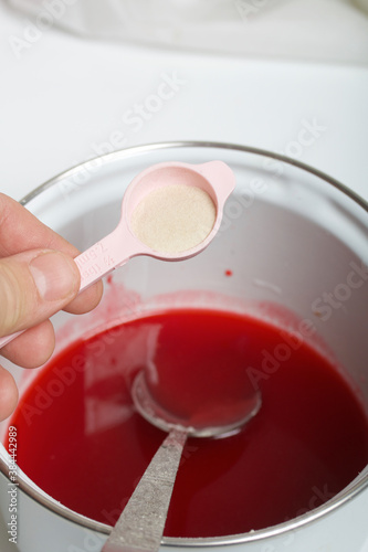 A woman makes jelly from raspberry syrup. Adds a spoonful of agar agar. Levington cake, stages of preparation.