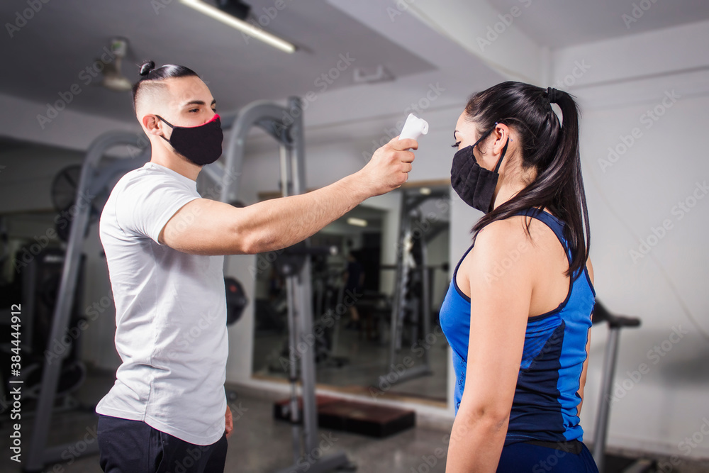 White man taking the temperature of a young caucasian girl in the gym. COVID-19 pandemic social distancing rules White man taking the temperature of a young caucasian girl in the gym. COVID-19 pandemic social distancing rules