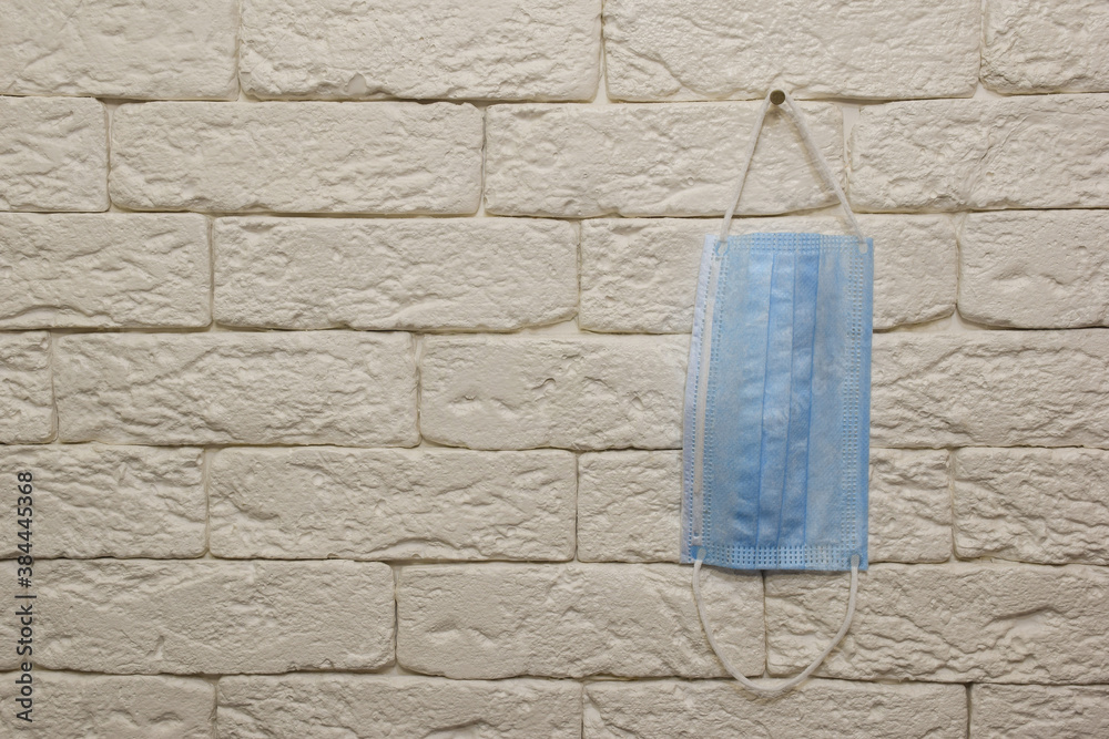 Fototapeta A blue medical mask hangs on a light brick wall on the right side. The left half of the wall is empty