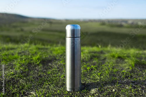 Close-up of steel stainless thermos on green grass.
