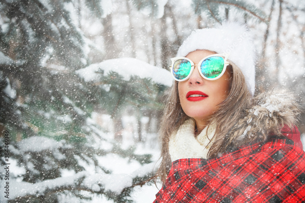 Outdoors lifestyle close up portrait of beautiful girl walking through the snowy spruce forest. Smiling and enjoying wintertime. Wearing stylish sunglasses, down jacket, hat. Wrapping in a blanket. I Outdoors lifestyle close up portrait of beautiful girl walking through the snowy spruce forest. Smiling and enjoying wintertime. Wearing stylish sunglasses, down jacket, hat. Wrapping in a blanket. I
