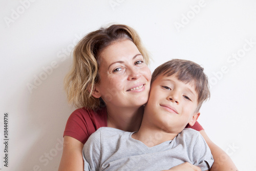 Portrait of happy smiling mom hugging her son sitting on a light background. Happy family concept. 