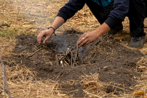 Man putting wooden sticks into fire. Bonfire in the forest. Campfire in a nature