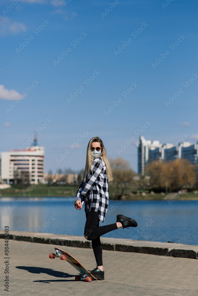 Portrait of a young female in a medical mask with longboard in the city during the quarantine