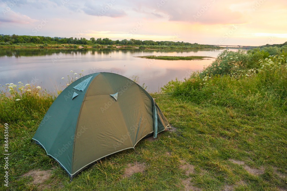 tourist tent is by the river in summer at sunset.