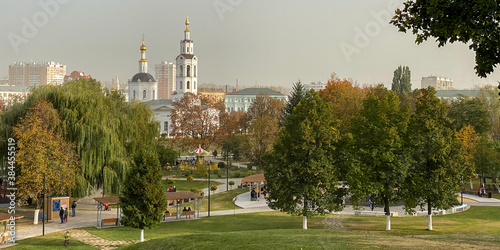 Panorama of the city's children's park with carousels green and yellow trees, in the background an old church and houses, mobile photo
