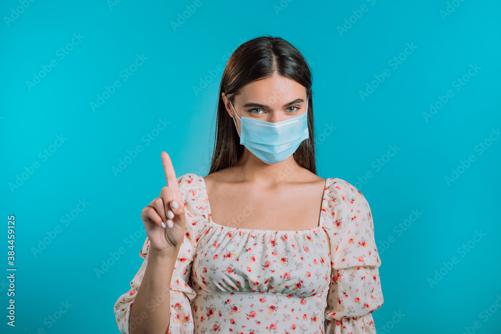 Young woman showing no finger, stop gesture. Girl in face medical mask during coronavirus pandemic. Portrait on blue background. Protection with respirator against COVID-19 outbreak Young woman showing no finger, stop gesture. Girl in face medical mask during coronavirus pandemic. Portrait on blue background. Protection with respirator against COVID-19 outbreak