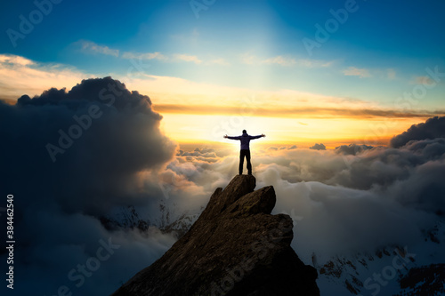 Adventurous Man Hiker With Hands Up on top of a Steep Rocky Cliff. Sunset or Sunrise. Landscape Taken from British Columbia  Canada. Concept  Adventure  Explore  Hike  Lifestyle. Composite.