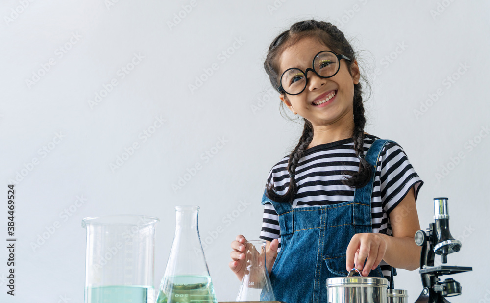 Little 6s cute girl smiling with microscope, laboratory bottle and water experiment study scientists while looking camera at school. Education science concept. Little 6s cute girl smiling with microscope, laboratory bottle and water experiment study scientists while looking camera at school. Education science concept.