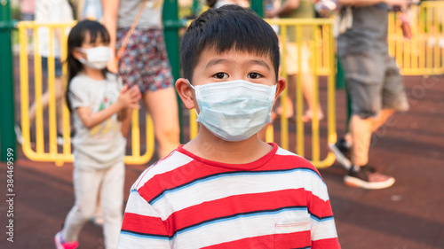 One young Asian boy student is wearing a surgical/disposal mask at the public park during covid-19 coronavirus pandemic, new normal concept.