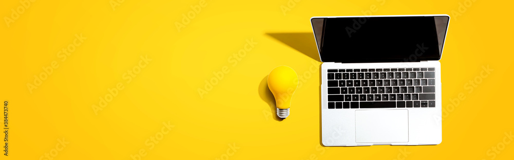 Laptop computer with a yellow light bulb from above - obrazy, fototapety, plakaty 
