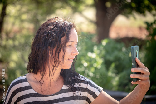 Woman sitting in beautiful garden location talking on smart phone video call © Caseyjadew